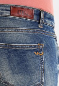 Blå denimjeans med en läderlapp som är märkt "LTB." Har orange sömmar, fem fickors design och subtil blekning på tyget.