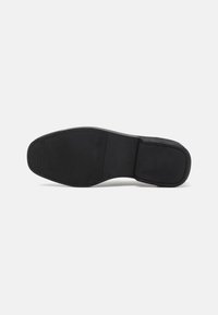 Schwarze Schuhsohle mit strukturierter Oberfläche, abgerundetem Zehenbereich und definiertem Absatz. Glatte Kanten und minimales Design für unkomplizierte Funktionalität.