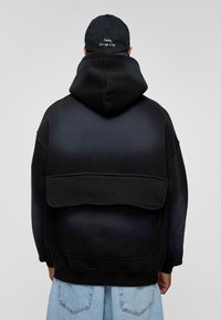 Zwarte gradient hoodie met een buidelzak en een grote kap. De stof lijkt zacht en het ontwerp heeft zichtbaar stiksel detail.