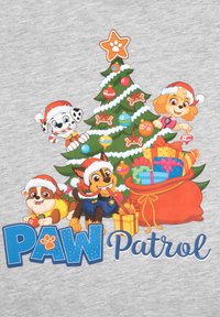 Grafica di Paw Patrol su una maglietta grigia che presenta cani cartoon con cappelli di Babbo Natale attorno a un albero di Natale carico di regali, decorazioni e un sacco rosso.