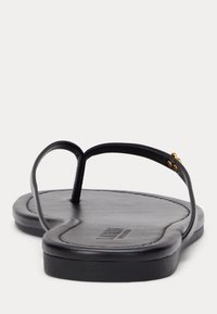 Sandale negre cu talpă plata, cu bretele subțiri și o talpă căptușită în formă de inimă, văzută din spate pe un fundal alb.