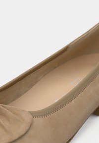 Μπεζ σουέτ παπούτσι με χαμηλό τακούνι, στρογγυλεμένη μύτη και ραμμένη επένδυση, με μερική εικόνα από πάνω και εσωτερική όψη.