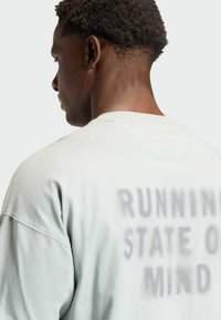 Lichtgroene oversized sweater met een zachte textuur, met de frase "RUNNING STATE OF MIND" in vervaagd grijs op de achterkant.