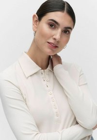 Pitkähihaisessa, vaaleanbeigeissä polo-paidassa on ribbikuviointi, napitettu etuosan läppä ja klassinen kaulus.