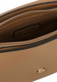 Innenraum einer tanfarbenen Ledertasche mit strukturierter Oberfläche, ausgestattet mit einem Reißverschlussfach und einem Druckknopfverschluss.