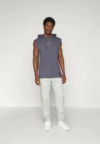 Sötét szürke, kapucnis, ujjatlan felső, kontrasztos oldalsávokkal; világosszürke melegítőnadrággal és fehér tornacipővel párosítva.