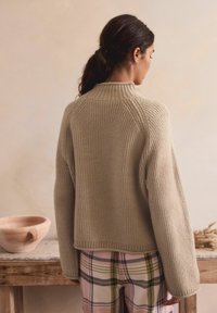 Beige ribbet striktrøje med høj krave og løs pasform, der har faldne skuldre. Sammen med bukser med ternet mønster i bløde farver.