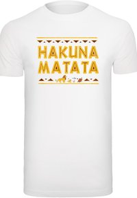 Hvit bomull T-skjorte med "HAKUNA MATATA" i gul, fet skrift, med dyreillustrasjoner og dekorative stammemønstre.