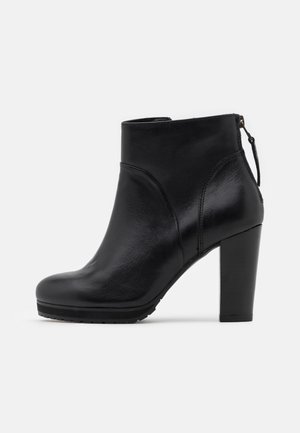 Bottine en cuir noir avec un talon carré et une fermeture éclair à l'arrière sur fond blanc, vue de côté.