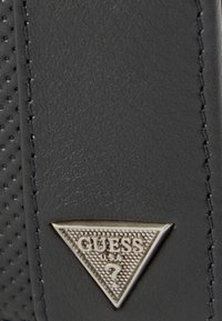 Mustast sünteetilisest materjalist tekstuurse pinnaga, millel on kolmnurkne hõbedane logo silt, millel on kirjas "GUESS" ja küsimärk.