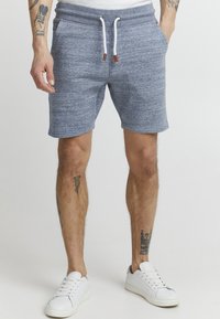 Shorts bleus chinés avec une taille élastique et un cordon de serrage blanc. Comprend des poches latérales et une coupe décontractée, associés à des baskets blanches.