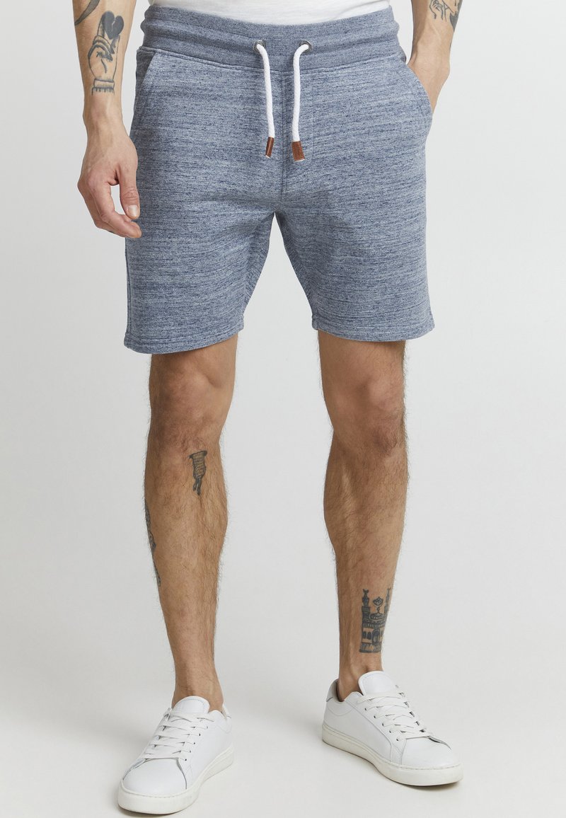 Shorts bleus chinés avec une taille élastique et un cordon de serrage blanc. Comprend des poches latérales et une coupe décontractée, associés à des baskets blanches.