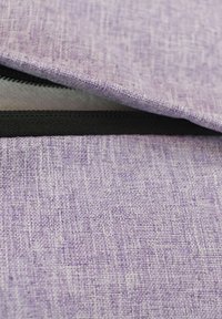 Lila tygpåse med en strukturerad yta. Har en svart dragkedja och en något vikit klaff som avslöjar det inre fodret. Hållbar design.