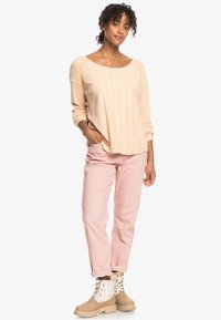 Beige textuur langemouwen top, roze rechte broek en tan laarzen met veters en geruite accenten.