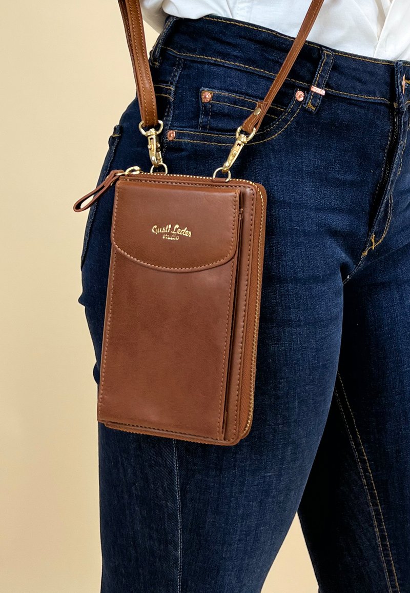 Bruine leren schoudertas met rits, voorzien van een voorvak, gouden hardware en een verstelbare schouderriem. Eenvoudig ontwerp.