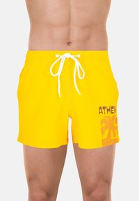 Shorts de bain jaunes avec une taille élastique à cordon de serrage, ornés d'un imprimé "ATHENS" en marron. Longueur courte et tissu lisse et léger.