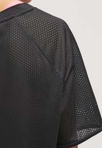 Sort sportstrøje med korte ærmer og perforeret tekstur, prydet med en pink kant ved halsen og rundet nederste kant for bedre ventilation.