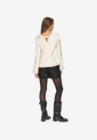 White satin top with keyhole detail, paired with a black sequined mini skirt and black knee-high boots. Smooth texture and fitted design.