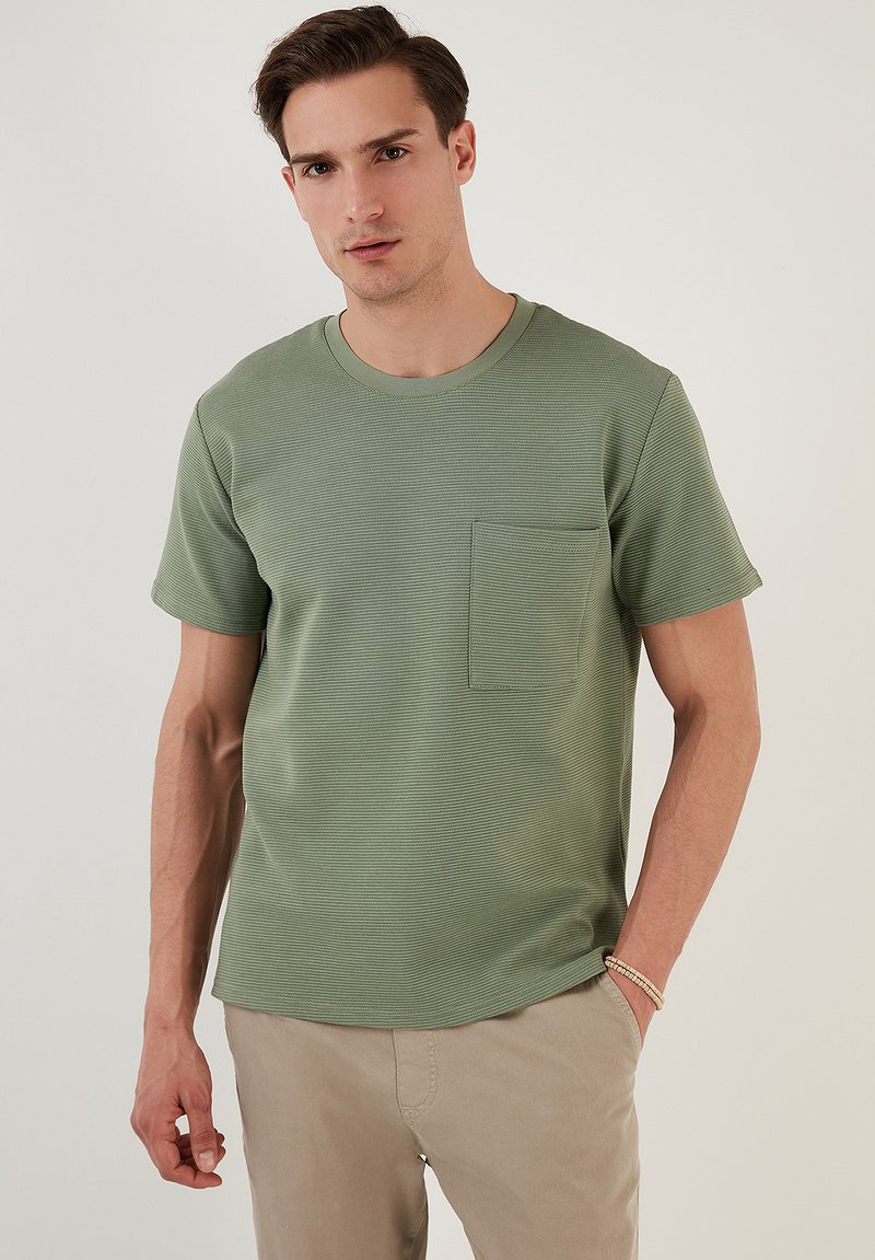 Maglietta verde a maniche corte in tessuto a costine, con scollatura rotonda e una piccola tasca sul petto. Design semplice e solido.
