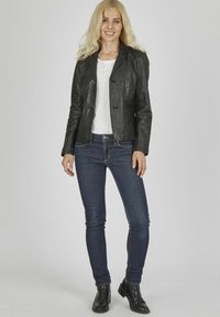Schwarze Lederblazer mit tailliertem Schnitt, einreihigem Design, zwei Knöpfen, kombiniert mit schlanken blauen Jeans und Stiefeletten.