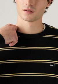 Maglione a righe nere con linee orizzontali gialle e grigie. Presenta un colletto a coste e un piccolo logo Levi's sul petto. Morbida texture in maglia.