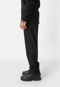 Zwarte geribbelde longsleeve shirt gecombineerd met zwarte taps toelopende broeken en stevige, gestructureerde zwarte sneakers met banddetails.