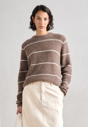 Braun gestreifter Pullover aus weichem, flauschigem Material mit weißen horizontalen Streifen. Hat einen runden Ausschnitt und gerippte Bündchen, kombiniert mit einem hellen Rock.