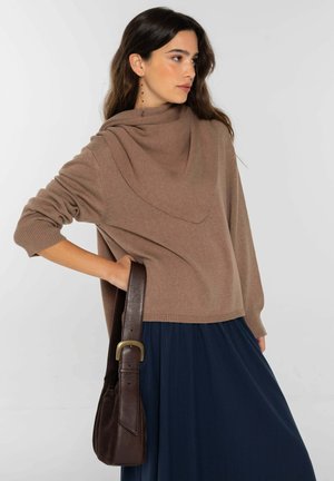 Suéter marrón de punto con escote drapeado, mangas largas y puños acanalados, combinado con un vestido azul marino y un bolso de cuero marrón.