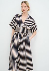Vestido a rayas en colores azul marino y beige claro, con mangas cortas, cuello con solapa, cintura ajustada y cierre frontal de botones con bolsillos.