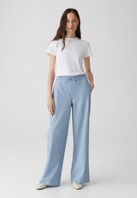 Pantalons larges bleu clair avec une taille élastique à cordon, associés à un t-shirt blanc uni à manches courtes et des ballerines beiges.