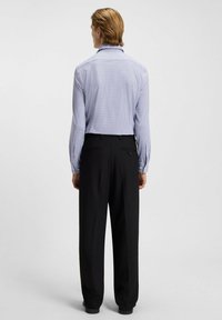 Bluse mit blauem Muster und langen Ärmeln, kombiniert mit hoch taillierten schwarzen Hosen. Die Bluse hat einen klassischen Kragen und geknöpfte Manschetten.