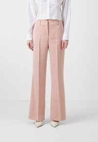 Lichtroze, hoge taille, wijde broek gemaakt van gladde stof, met voorplooien en een getailleerde pasvorm, gecombineerd met een witte blouse en puntige schoenen.