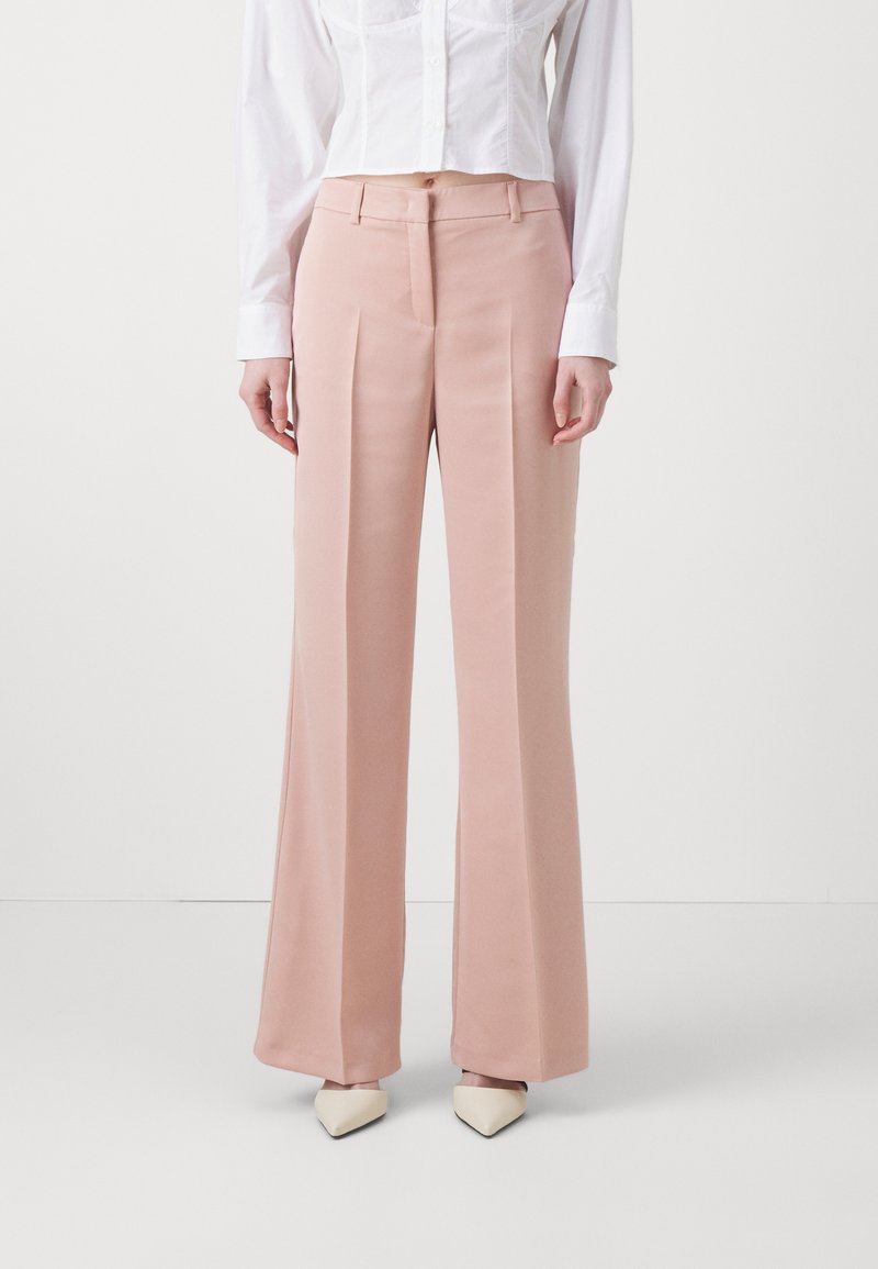 Lichtroze, hoge taille, wijde broek gemaakt van gladde stof, met voorplooien en een getailleerde pasvorm, gecombineerd met een witte blouse en puntige schoenen.
