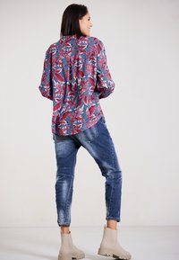 Floral blouse in blue, red, and white; relaxed fit, long sleeves, curved hem. Paired with distressed blue jeans and beige ankle boots.