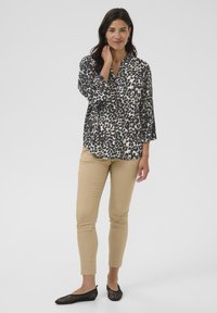 Leichte Bluse mit langen Ärmeln im schwarz-beigen Leopardenmuster, kombiniert mit schmalen beigefarbenen Hosen und schwarzen Mesh-Ballerinas.