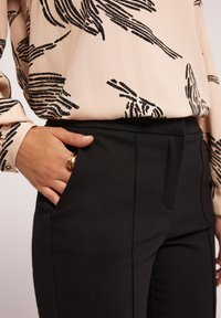 Bluzka z miękkiego, beżowego materiału z czarnym abstrakcyjnym wzorem; zestawiona z dopasowanymi czarnymi spodniami z kieszeniami bocznymi i gładką fakturą.