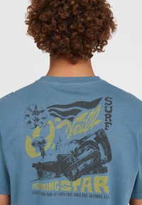 Blauwe katoenen t-shirt met een grafische print op de achterkant met een surf thema, die golven en een figuur toont, met gele en zwarte accenten.