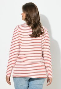 Langärmliges Oberteil aus weißem Stoff mit roten horizontalen Streifen. Verfügt über einen rund ausgeschnittenen Ausschnitt und eine lockere Passform, kombiniert mit hellblauen Jeans.