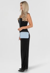 Borsa a tracolla blu chiaro con una texture liscia, forma rettangolare, accessori in metallo argentato e un dettaglio a frangia. Cintura regolabile inclusa.