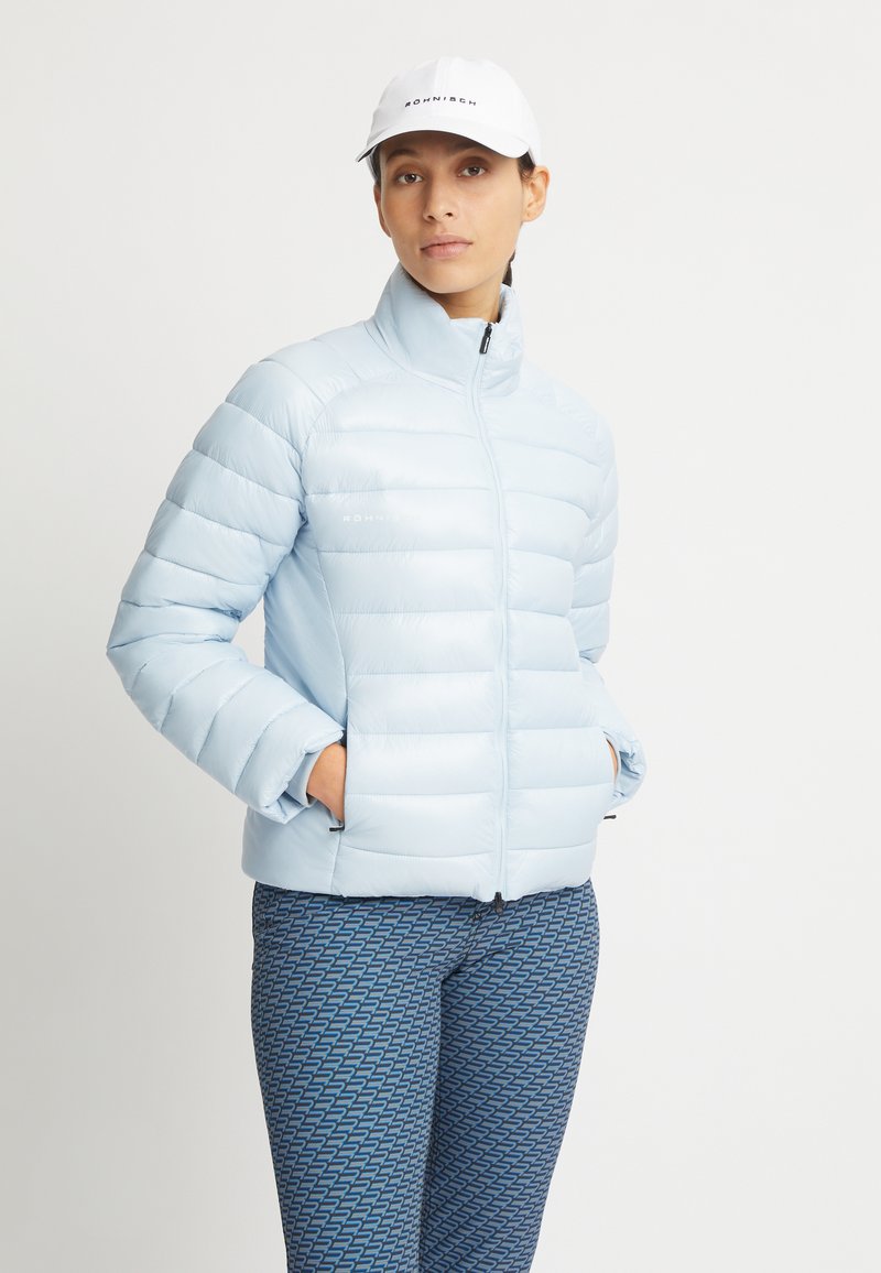 Chaqueta de plumas azul claro con cuello alto y costuras horizontales. Combinada con pantalones azules estampados que presentan un diseño geométrico.