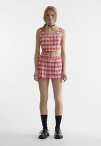 Rød og hvit rutete crop top med rett halslinje, kombinert med matchende mini nederdel. Modellen bruker svarte sokker og sko. Glatt stofftekstur.