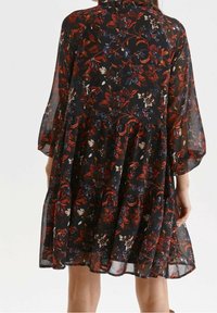 Svart blommig klänning med ett lätt, genomskinligt tyg med mönster av röda och blå blommor, långa ärmar och en lager-på-lager fåll.