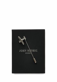Silverfärgad brosch med flygplansdesign, placerad på en lång nål. Presenterades i en svart låda med "JOHN HENRIC SWEDEN" präglat i silver.