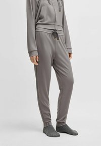 Grey jogger pants made of soft fabric, featuring a drawstring waist, side stripes, and ribbed cuffs. Worn with grey socks.
