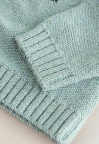 Manches d'un pull tricoté bleu clair avec poignets côtelés, mettant en valeur un tissu en laine doux et texturé en gros plan.