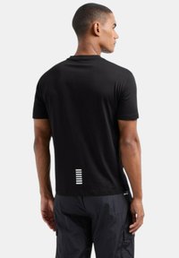 Maglietta nera a maniche corte realizzata in cotone. Presenta un design minimalista con accenti di striscia bianca sul retro. Tessuto semplice, vestibilità comoda.