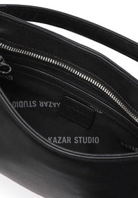 Svart läderhandväska med en slät yta, försedda med ett silverfärgat dragkedjestängning och ett foder i tyg som visar varumärket.