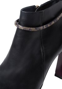 Svart läderankelstövel med en blank yta, prydd med en smyckad accentband nära toppen och en stabil klack.