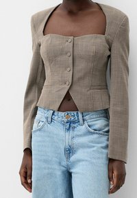 Brun rutigt kort kavaj med fyrkantig halsringning, långa ärmar och fem knappar, kombinerat med ljusblå högmidjade jeans.