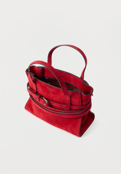 Τσάντα χειρός από κόκκινο σουέντ με διπλές λαβές, ζώνη λεπτομέρεια γύρω από το μπροστινό μέρος και κλείσιμο με κορυφαίο φερμουάρ πάνω σε απλό φόντο.